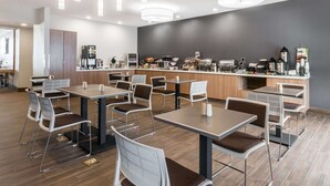 Un café moderno con varias mesas y sillas, una barra de café con distintos equipos, y una paleta de colores neutros.