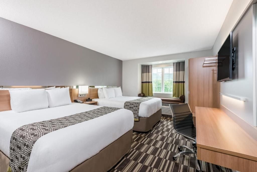 A hotel room with two beds, a desk, a TV, and a window with curtains.