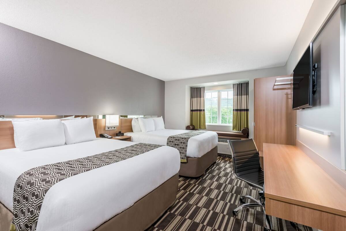 Une chambre d’hôtel avec deux lits, un bureau, une télévision et une fenêtre avec des rideaux.