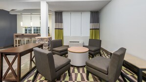Un espacio de descanso moderno con una mesa redonda, cuatro sillones grises, una mesa de centro de madera y una pared de acento de piedra.