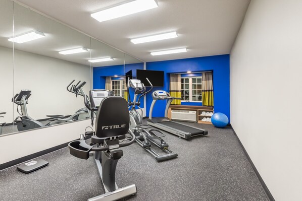 Un gimnasio con equipo cardiovascular, una cinta de correr y un espejo grande.