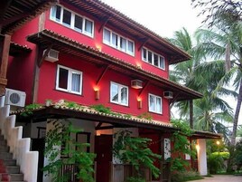 A two-story building with a red facade, multiple windows, and a covered porch with plants.
