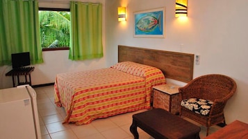 A room with a bed, a chair, a small table, a television, and a window with curtains.