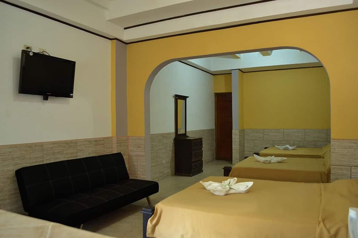 A hotel room with a sofa, two beds, a TV, and a fireplace.