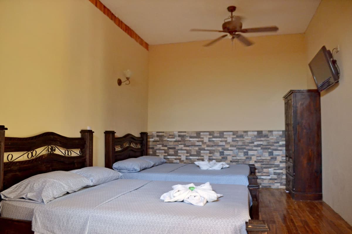 A hotel room with two beds, a wooden headboard, a stone-patterned wall, a ceiling fan, and a wooden cabinet.
