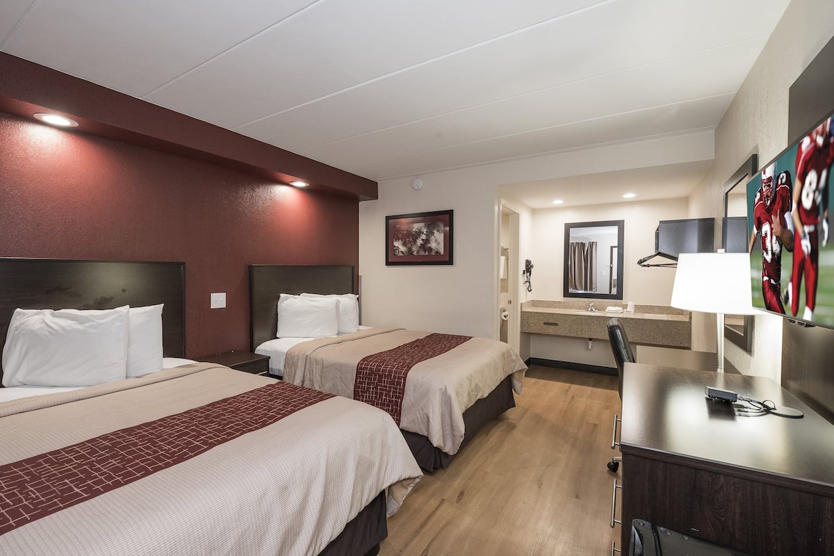 A hotel room with two beds, a desk, a chair, a TV, and a mirror.