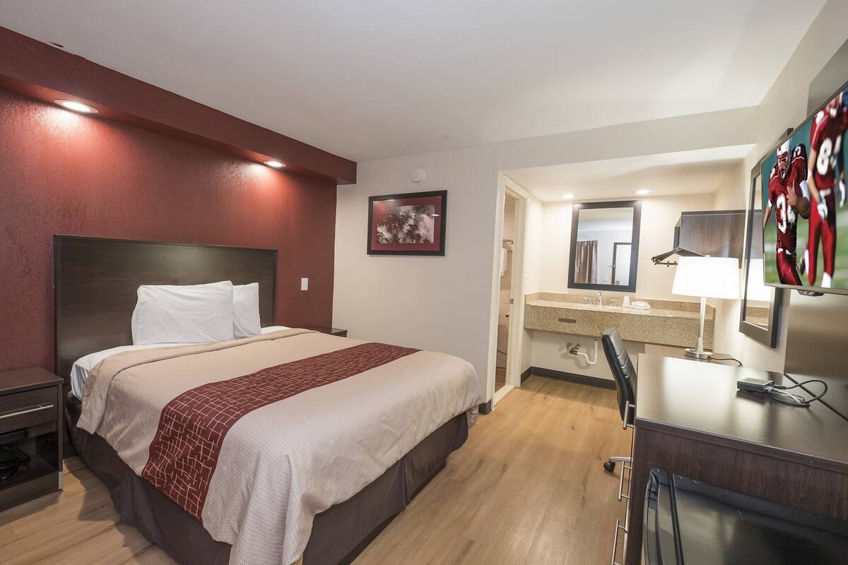 A hotel room with a bed, a desk, a mirror, and a bathroom visible through an open door.