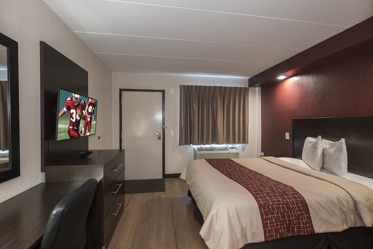 A hotel room with a bed, a TV, a desk, and a window with curtains.