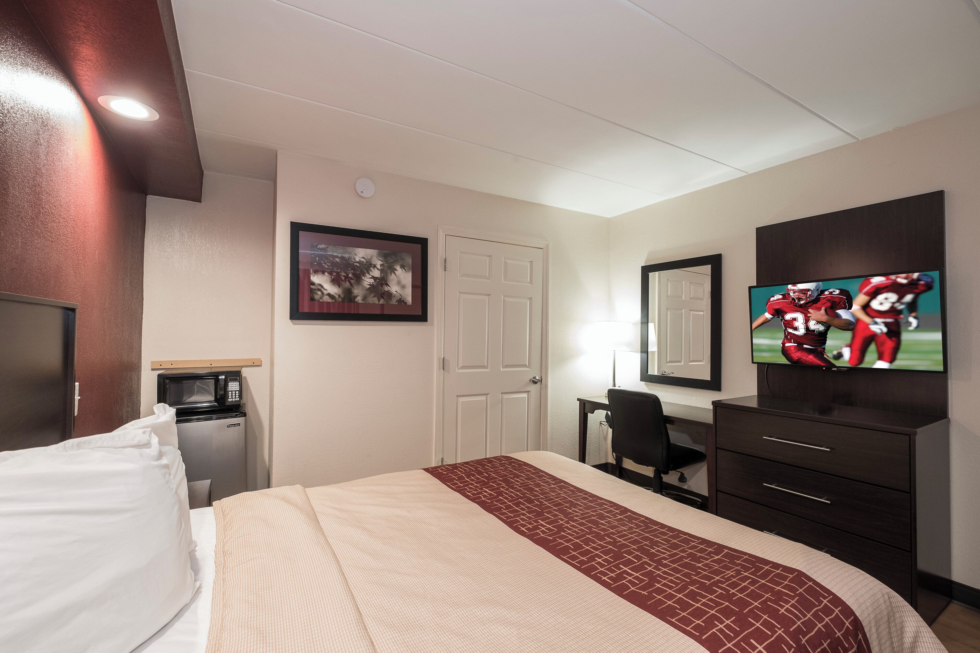Ein Hotelzimmer mit Bett, Schreibtisch, Fernseher, Mikrowelle und einer Tür.
