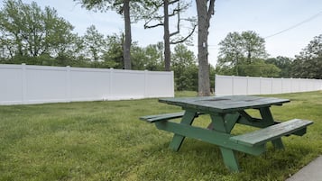 A picnic table in a grassy area with white fences and trees in the background.