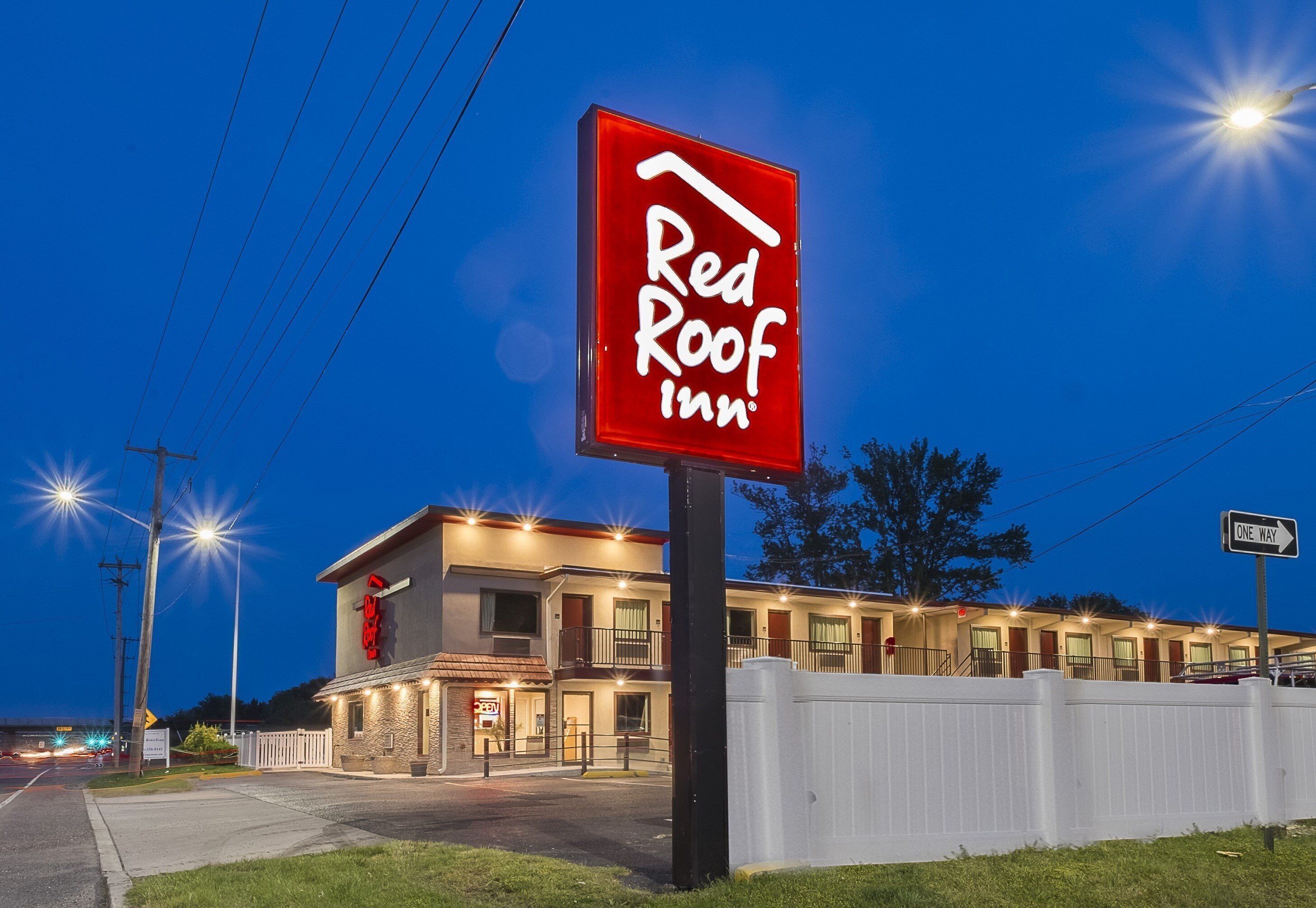 Un hôtel Red Roof Inn reconnaissable à son grand panneau rouge, à son bâtiment bien éclairé et à son parking délimité par une clôture.