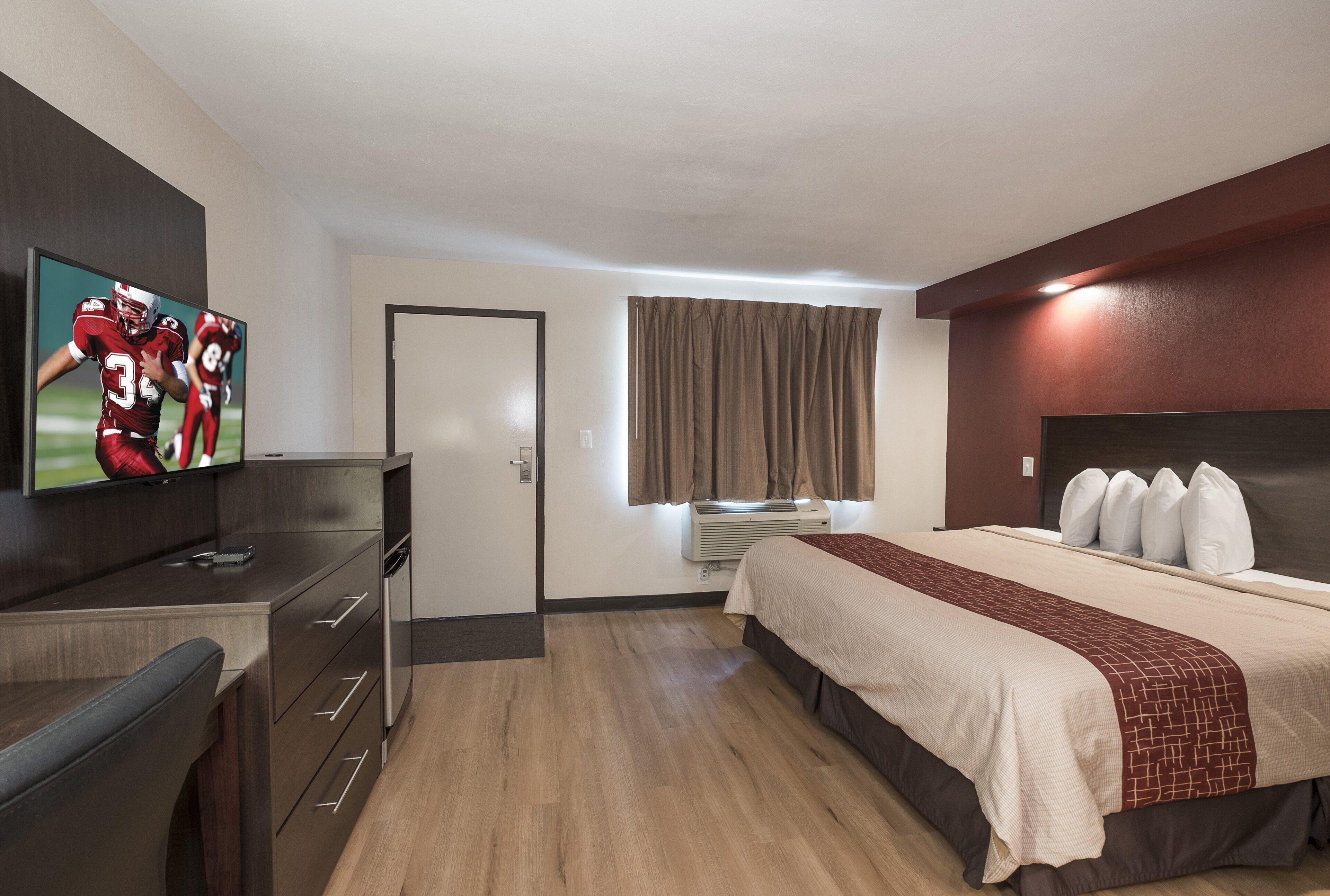 A hotel room with a bed, a desk, a television, and a window with curtains.