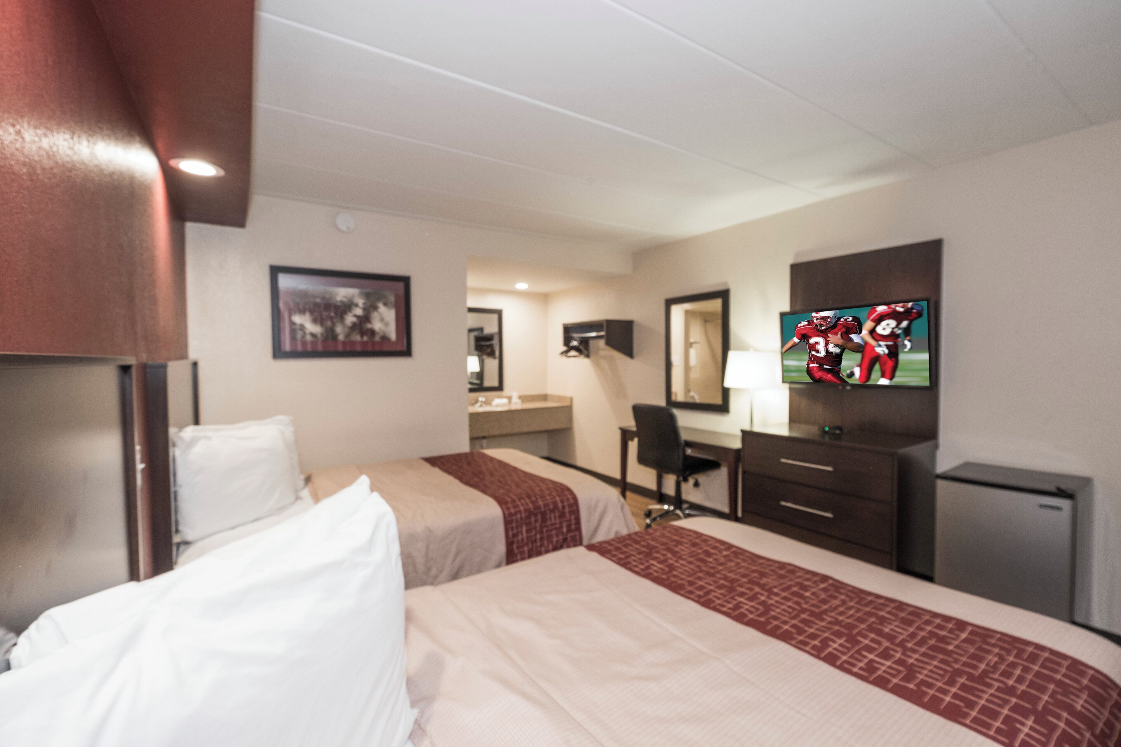 Habitación de hotel con dos camas, un escritorio, televisor y un refrigerador pequeño.