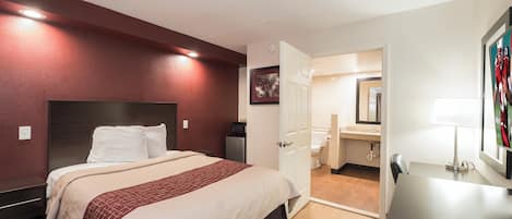 A hotel room with a bed, bedside table, and a bathroom visible through an open door.