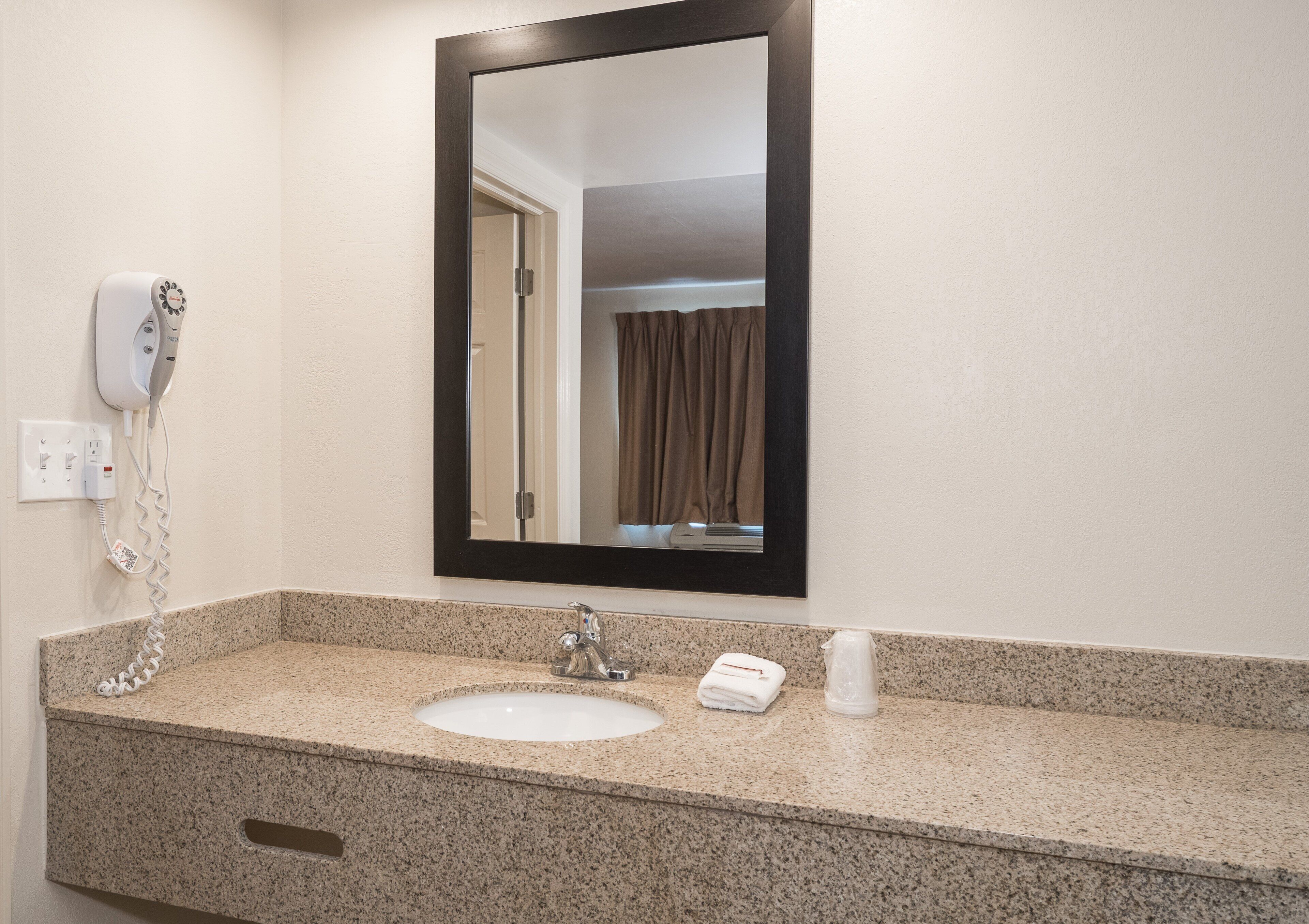 A bathroom with a granite countertop, a sink, a mirror, a towel dispenser, and a hairdryer.
