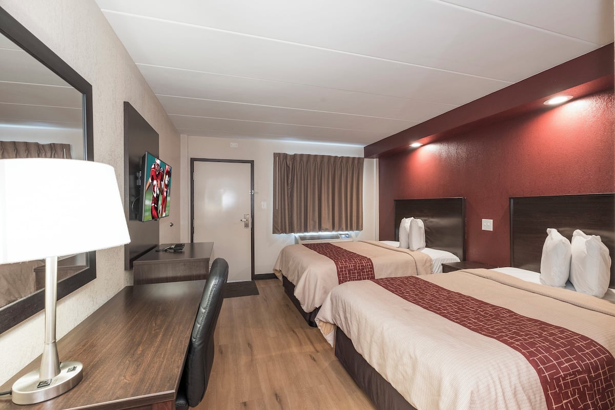 A hotel room with two beds, a desk, a chair, a TV, and a window with curtains.
