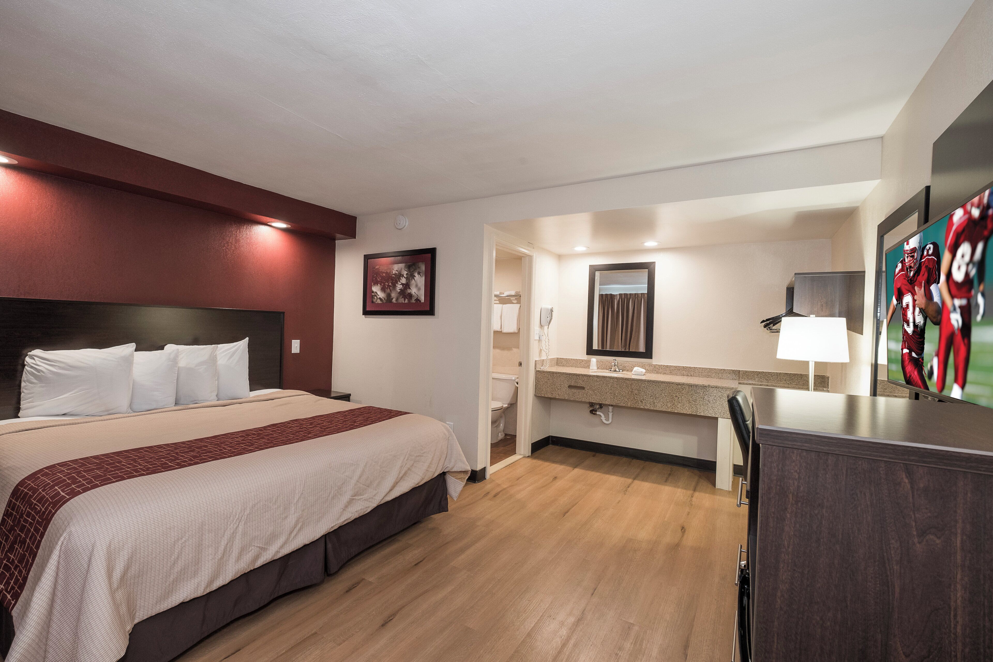 A hotel room with a bed, a desk, a mirror, and a bathroom visible through an open door.