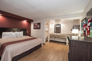 Una habitación de hotel con una cama, un escritorio, un espejo y un baño visible a través de una puerta abierta.