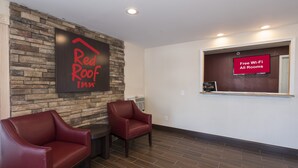 A Red Roof Inn lobby with a stone wall, two leather chairs, a flat-screen TV, and a sign stating "Free Wi-Fi All Rooms". - Red Roof Inn Wildwood - Cape May/ Rio Grande (Rio Grande)