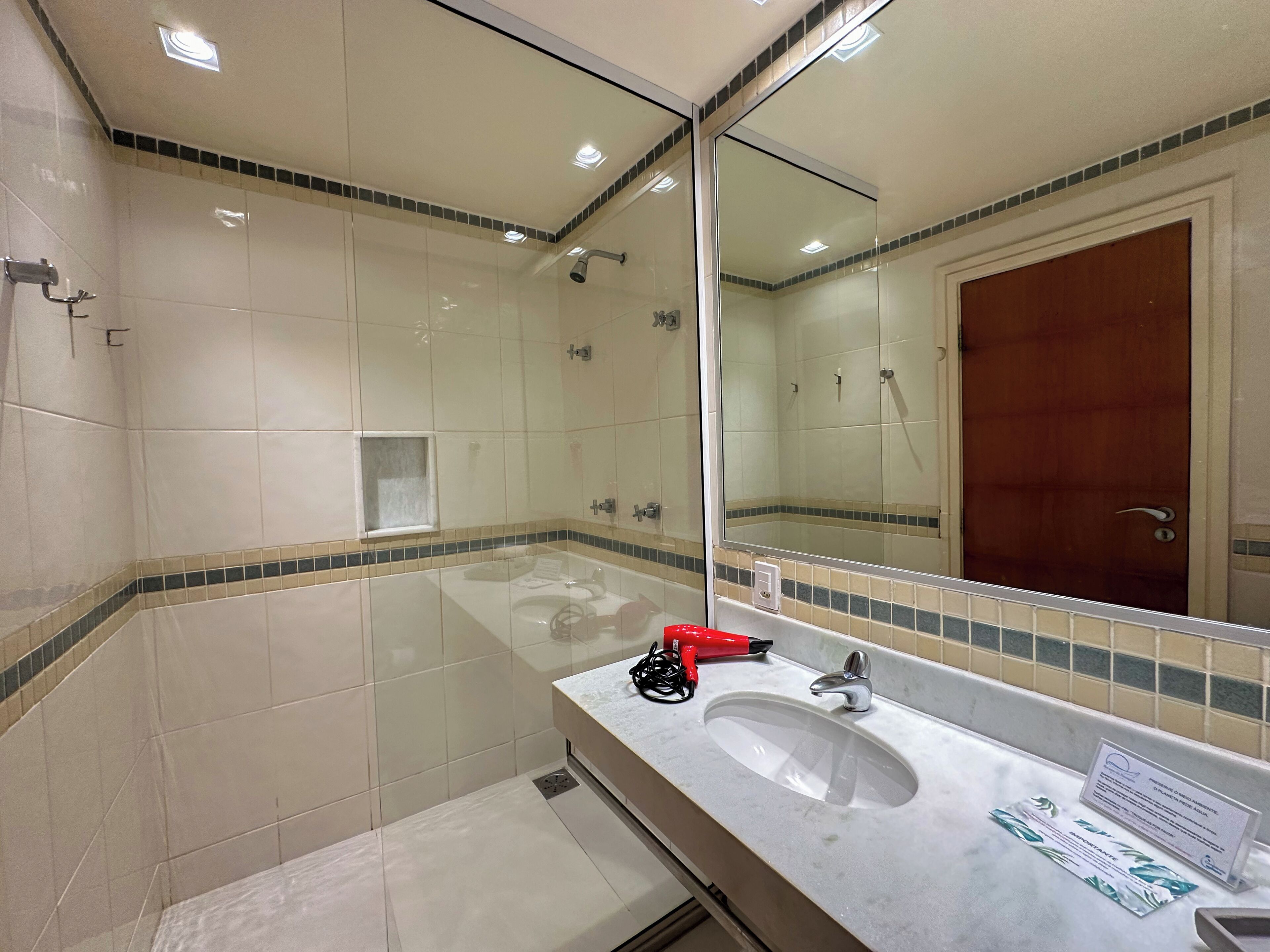A bathroom with a large mirror, a sink, and a shower.