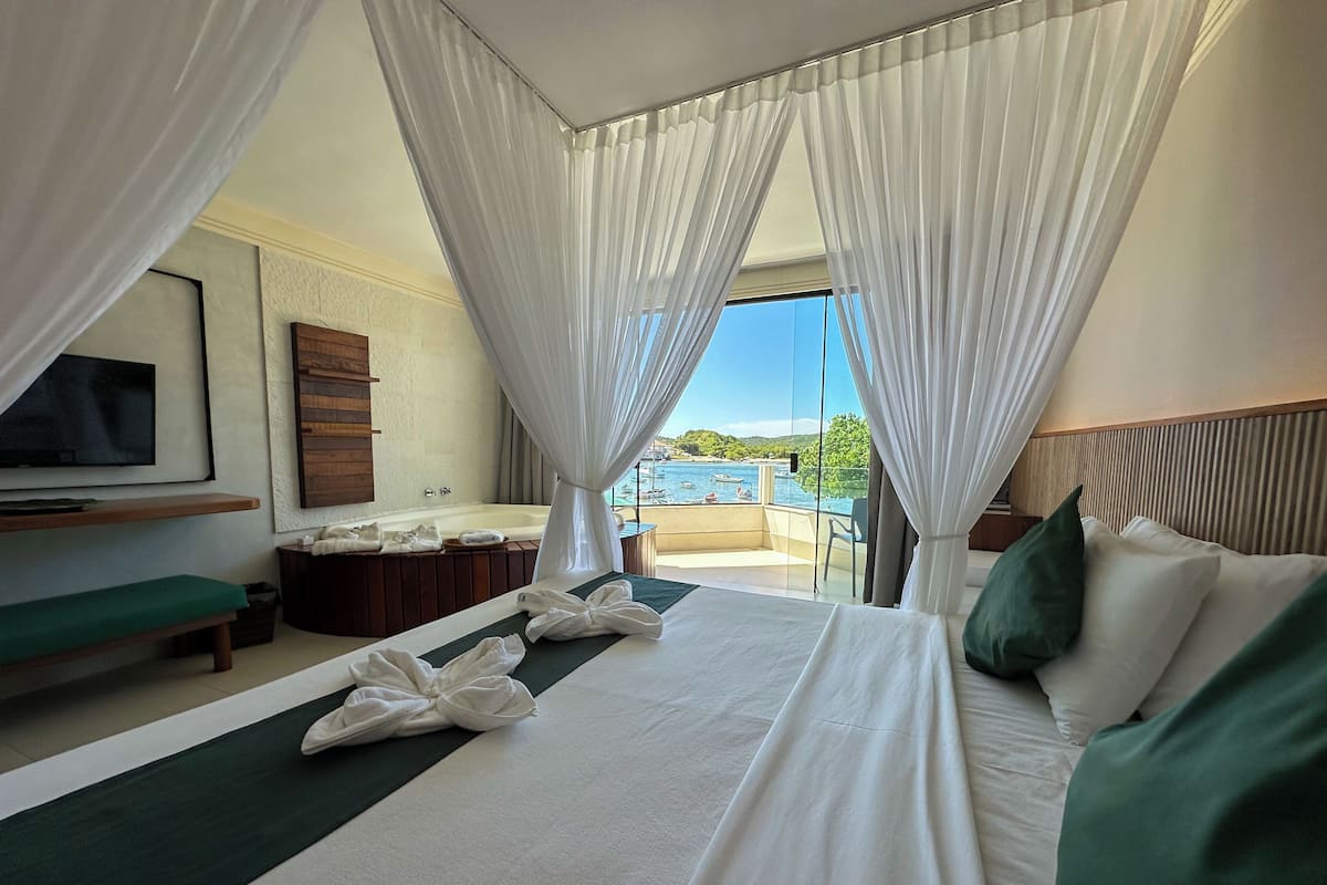 Une chambre d’hôtel avec un lit, un banc, une télévision, une baignoire et une vue sur la mer.