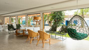 Een ruime binnenruimte met rieten stoelen, een hangstoel en een bank met kussens.