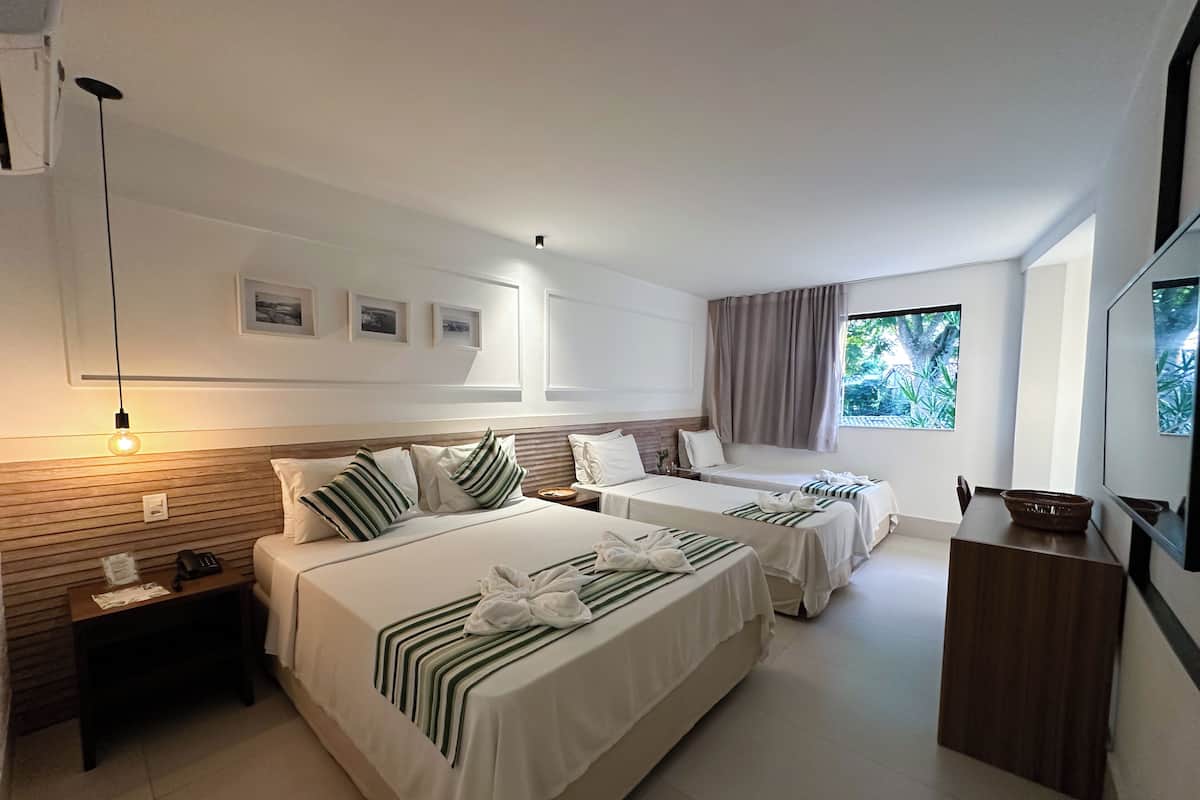 Une chambre d’hôtel avec deux lits, une table de chevet avec un téléphone, un bureau avec un bol, et une fenêtre donnant sur un paysage verdoyant.
