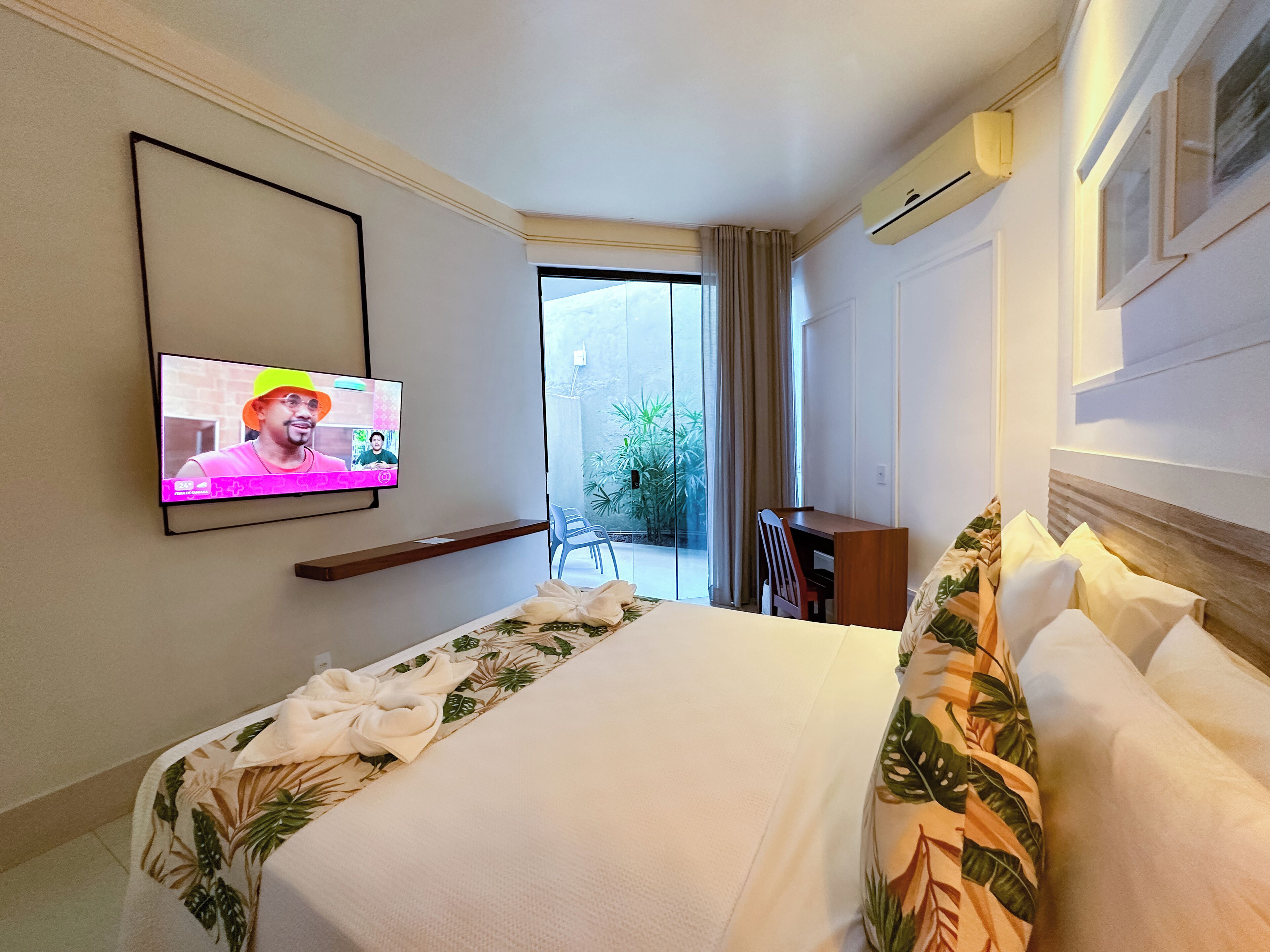 A hotel room with a bed, a desk, a television, and a view of the outdoors.