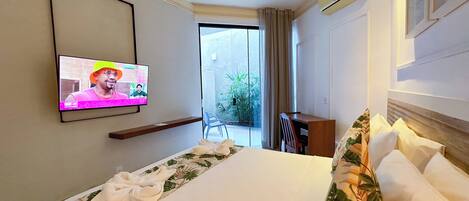 A hotel room with a bed, a desk, a television, and a view of the outdoors.