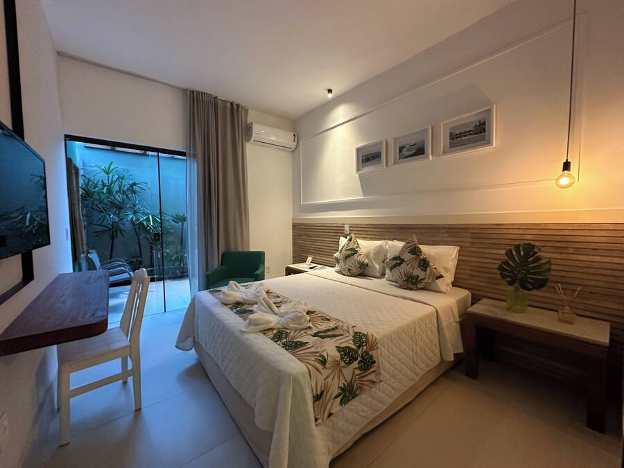 Une chambre d’hôtel moderne dotée d’un grand lit, d’un bureau, d’une chaise, d’un balcon agrémenté de plantes et d’une télévision.