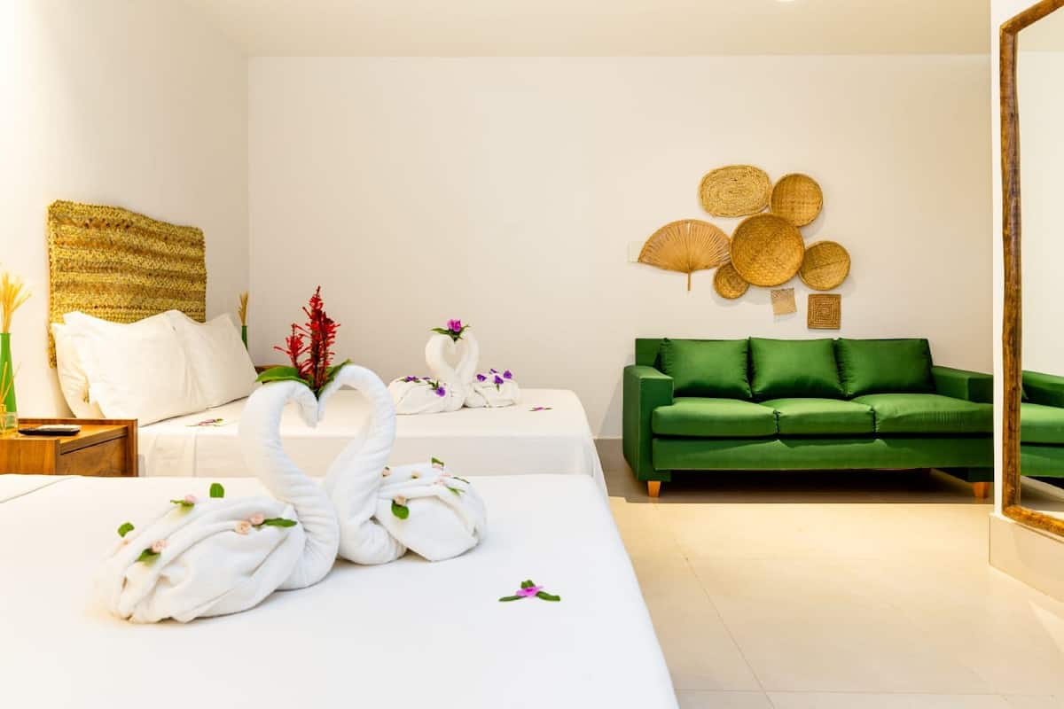Une chambre d’hôtel avec un lit, un canapé vert, un mur décoré de paniers tressés et un miroir.