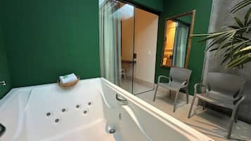 Un baño moderno con una bañera grande, cabina de ducha con mampara de cristal y zona de estar con sillas.