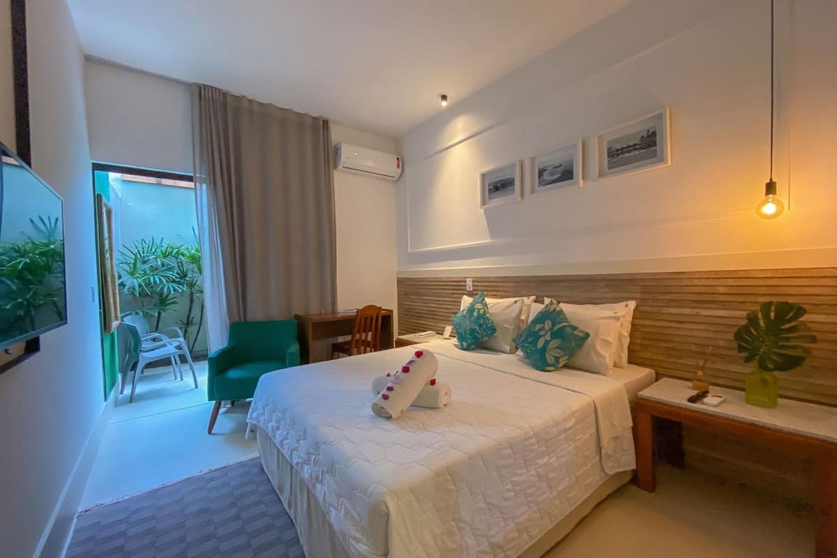 Une chambre d’hôtel avec un lit, un bureau, une chaise, une télévision et une fenêtre avec des rideaux.