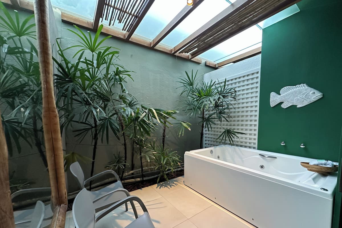 Une salle de bain moderne avec une grande baignoire, des murs verts et plusieurs plantes en pot.