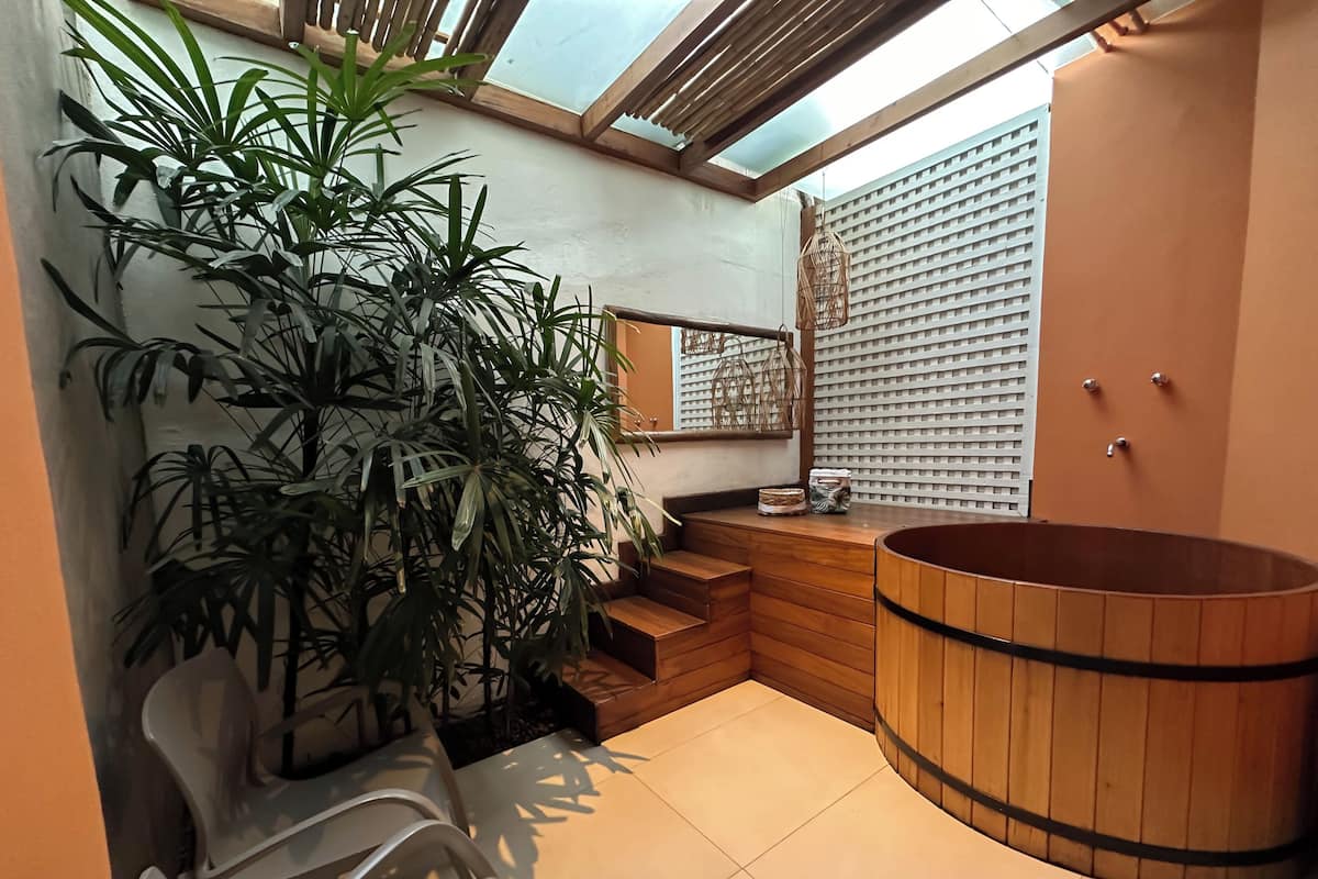Une salle de bain moderne avec une baignoire en bois, une grande plante en pot et un coin salon avec des fauteuils.