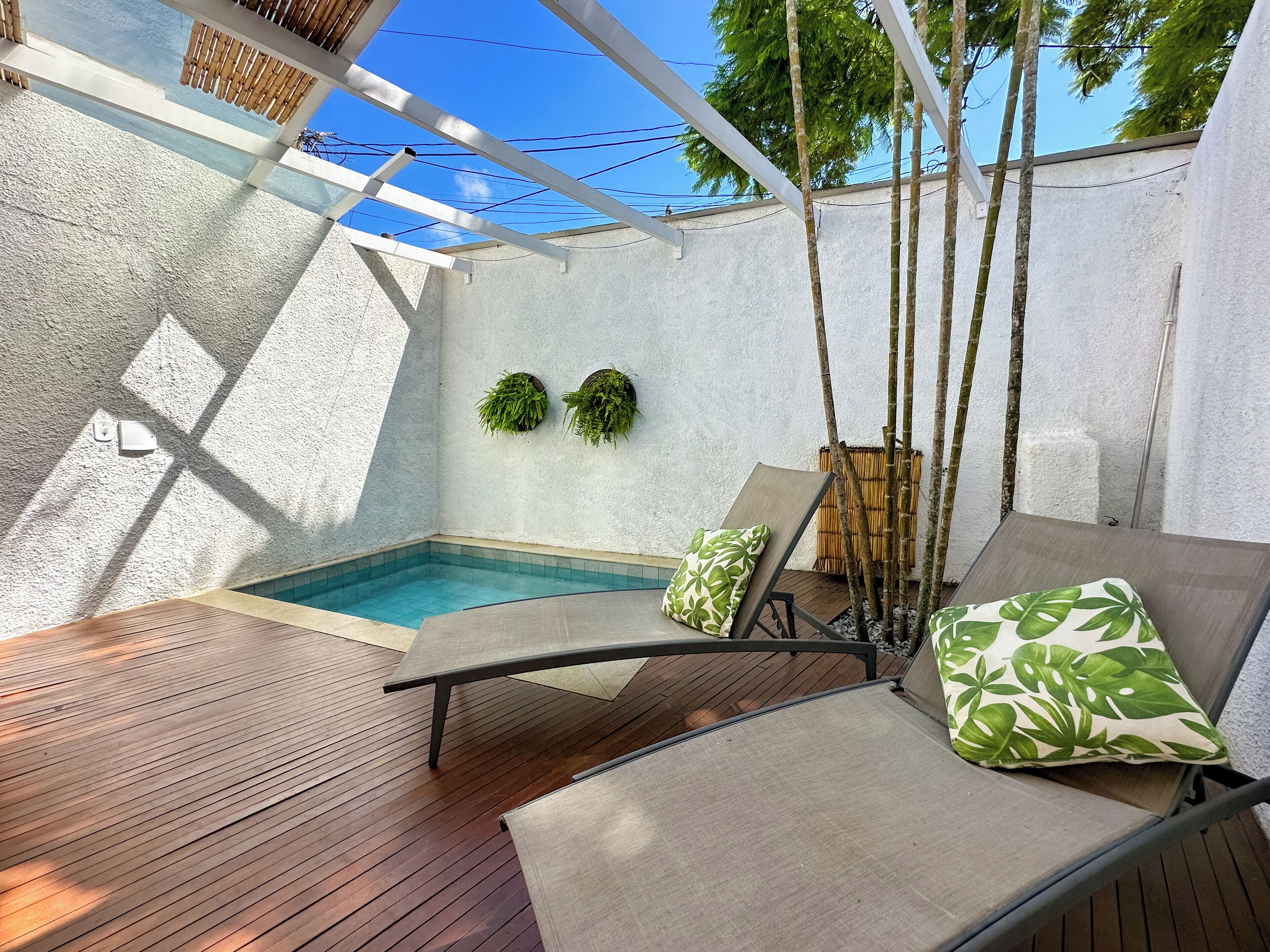 A poolside area with a wooden deck, a lounge chair with cushions, and a small pool.