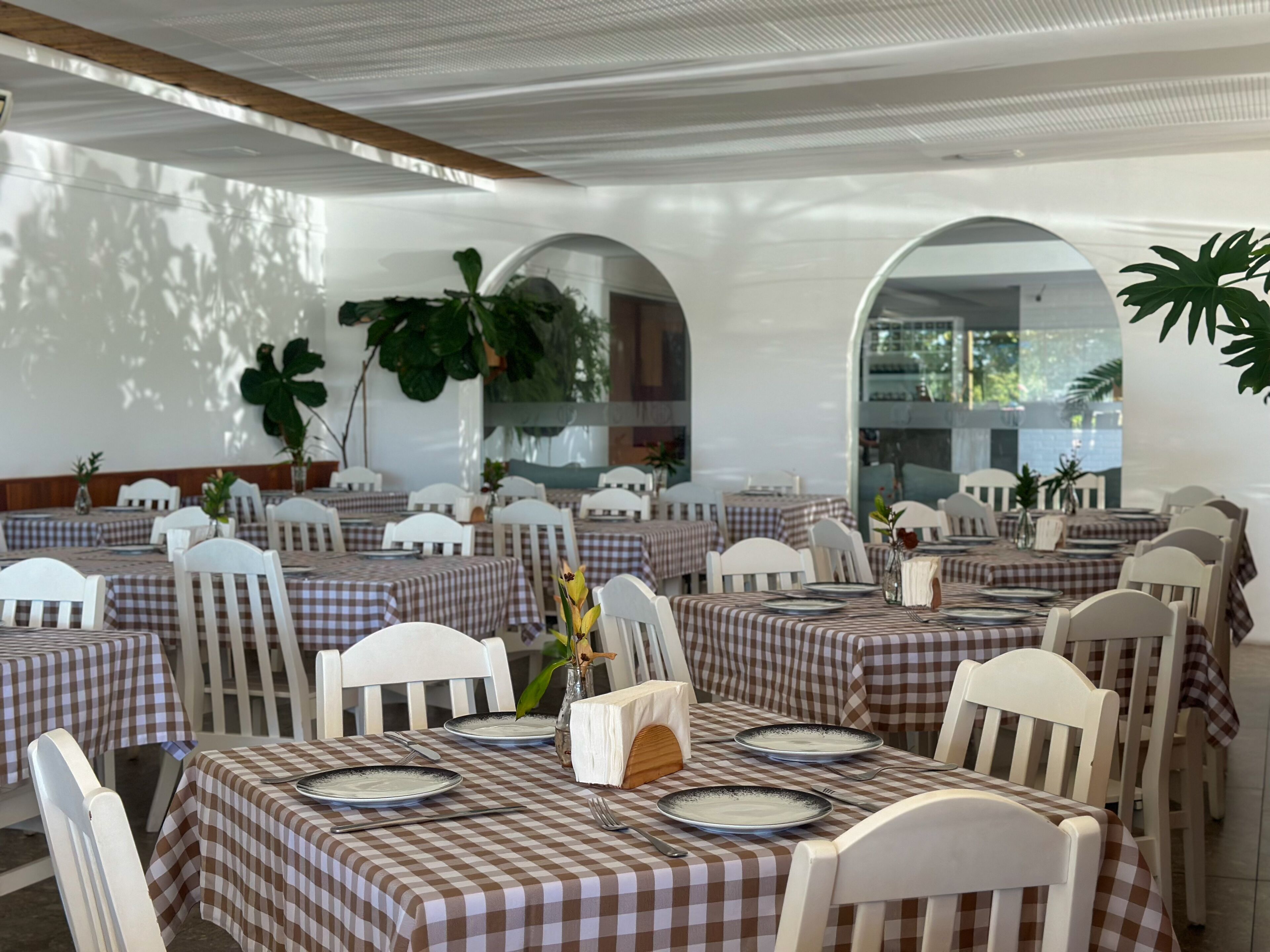 A restaurant with checkered tablecloths, white chairs, and potted plants.