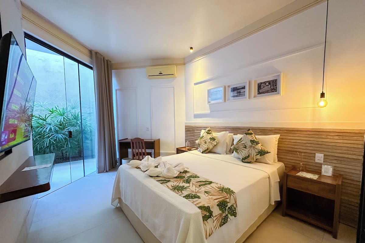 Une chambre d’hôtel avec un grand lit, un bureau et une télévision. Elle dispose d’un balcon agrémenté de plantes et offrant une vue sur l’extérieur.