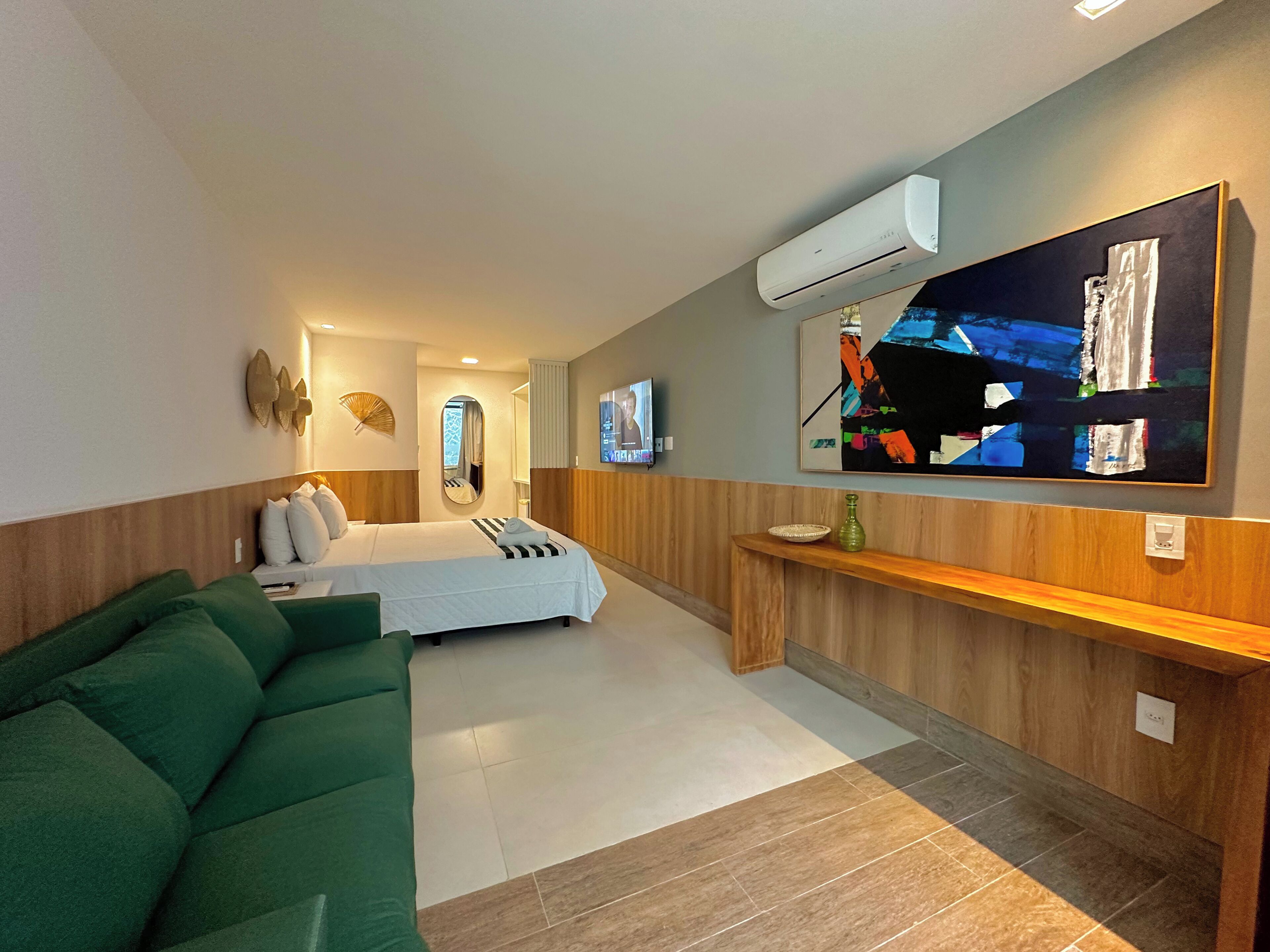 Ein modernes Hotelzimmer mit einem Bett, einem grünen Sofa, einem Fernseher und einer Klimaanlage.