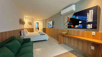 Ein modernes Hotelzimmer mit einem Bett, einem grünen Sofa, einem Fernseher und einer Klimaanlage.