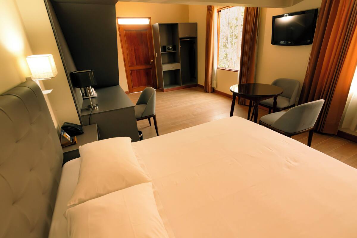 Ett hotellrum med en säng, ett skrivbord med en stol, en tv och ett litet bord med en stol.