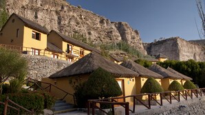 A row of yellow buildings with thatched roofs, stone walls, and a staircase leading up to them. - El Refugio Hotel Colca (Chivay)