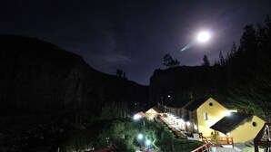 A mountain lodge with a staircase leading to a yellow building, surrounded by trees and illuminated by night lights. - El Refugio Hotel Colca (Chivay)