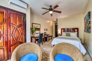 Quarto de hotel com duas camas, uma escrivaninha, uma cadeira, um ventilador de teto e um ar condicionado.