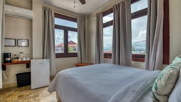 Hotelkamer met een bed, een bureau met koffiezetapparaat, een koelkast en grote ramen met gordijnen.