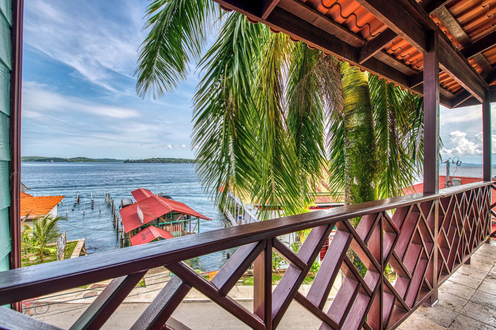Un balcón de madera con vista al mar y palmeras.