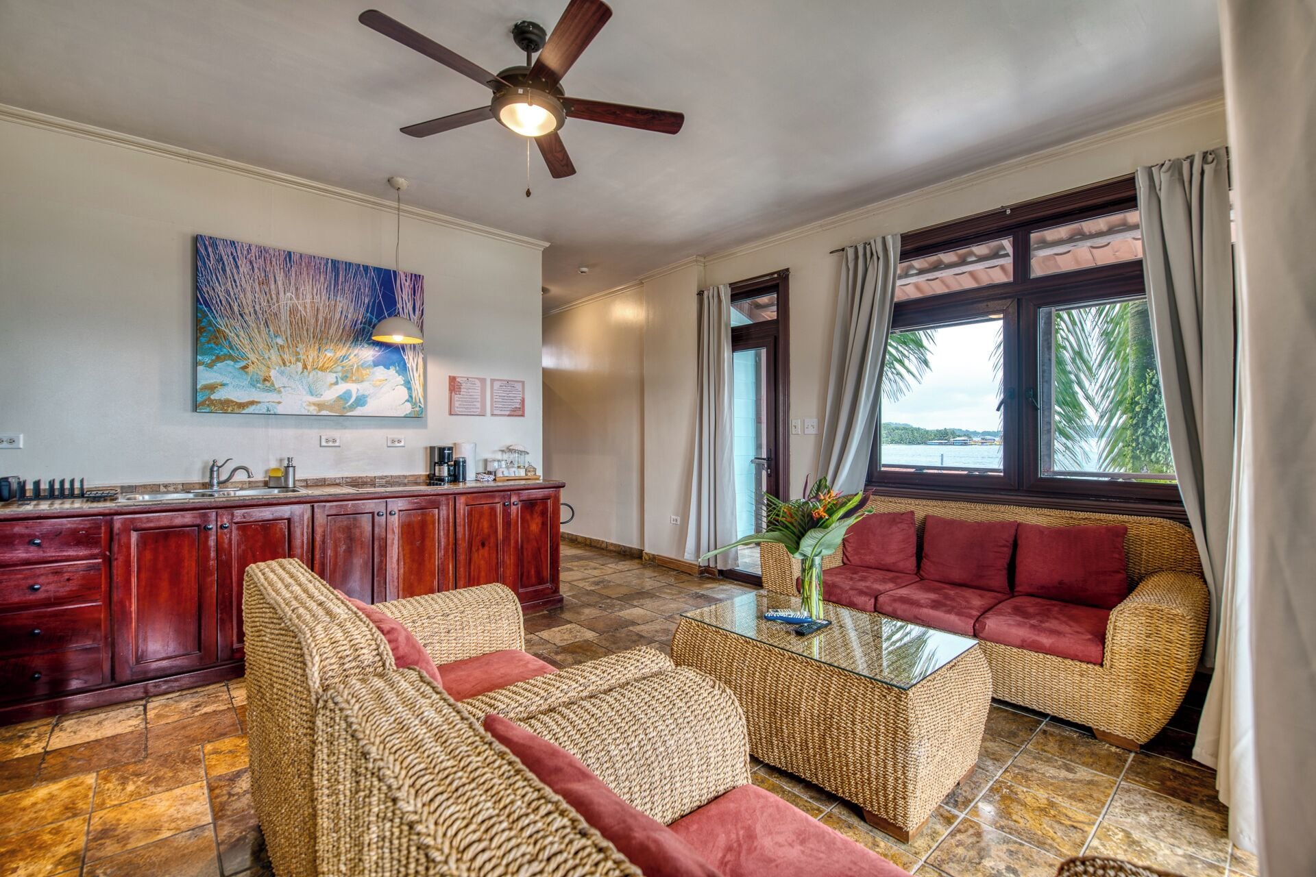 A room with a ceiling fan, a dining area with a wooden bar, a sofa, and a view of the outdoors.