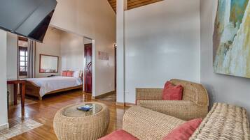A modern hotel room with a bed, a wicker sofa, a round ottoman, and a large painting on the wall.