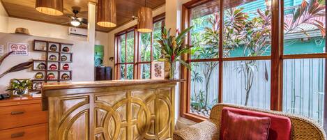 Un área de recepción con mostrador de madera, muebles de mimbre y vistas a plantas tropicales a través de grandes ventanales.