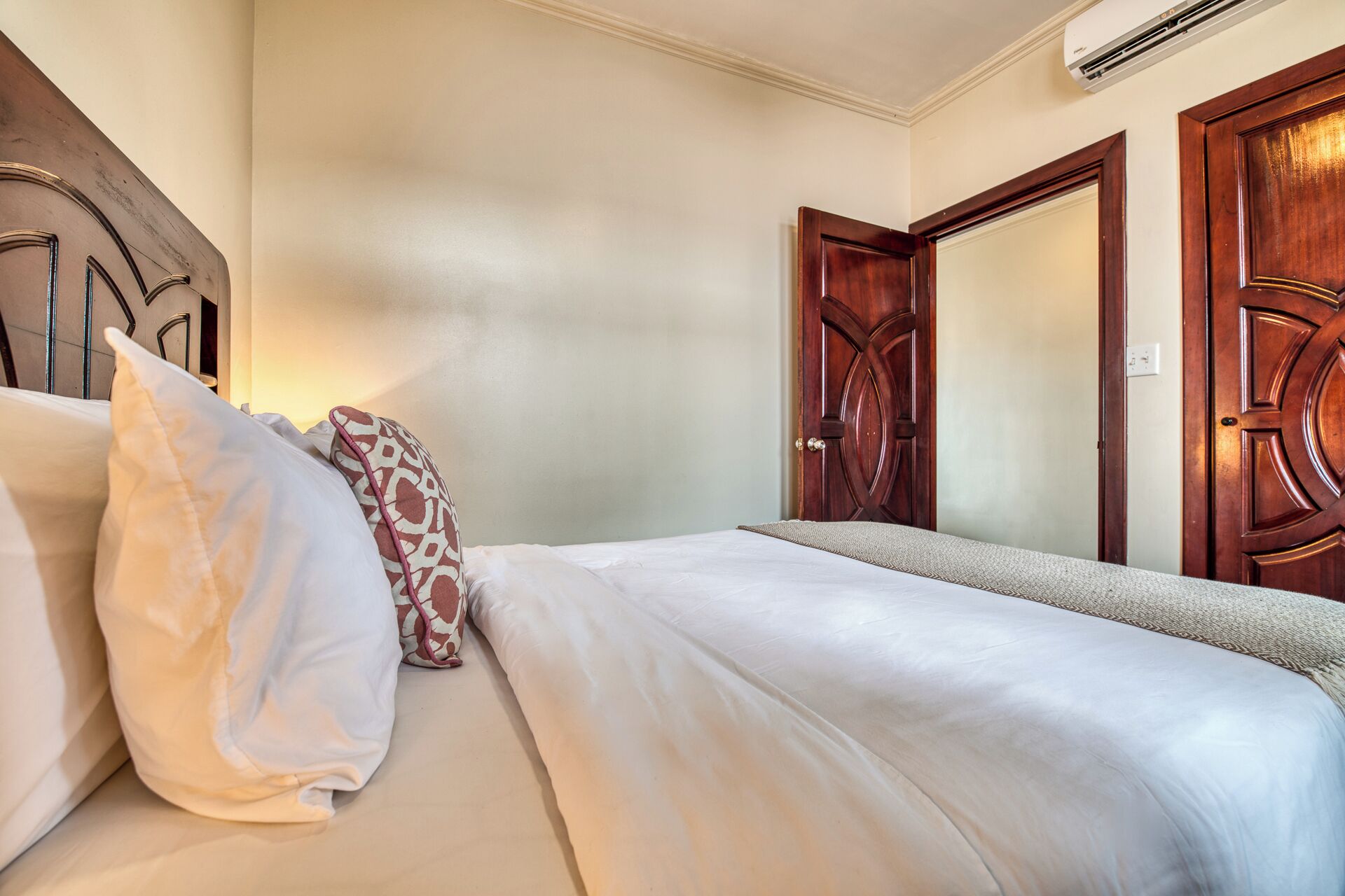 A hotel room with a bed, pillows, a wooden door, and an air conditioning unit.